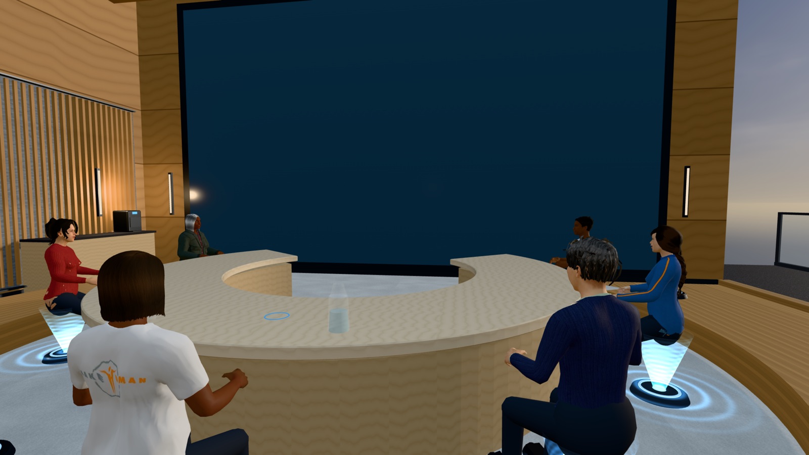 Avatars in different outfits seated around the curved table, seen from across the room